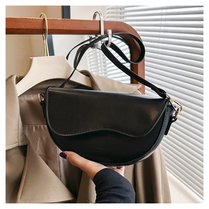 Détail d'un sac besace noir en cuir avec boucles dorées suspendu sur un trench-coat chic