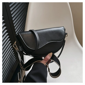 Détail du sac selle en cuir noir avec rabat asymétrique et large bandoulière tissée