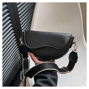 Détail du sac selle en cuir noir avec large bandoulière tissée et boucle dorée