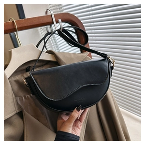 Détail du sac selle en cuir mat noir avec rabat ondulé et logo gaufré élégant