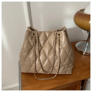 Detail of beige quilted bucket bag with golden chain strap on a wooden cabinet