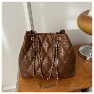 Detail of dark brown quilted PU leather bucket bag with gold chain on wooden table