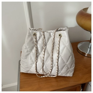 Detail of white quilted faux leather bucket bag with gold chain strap in home setting