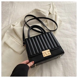 Détail d'un sac bandoulière matelassé noir avec fermoir doré sur un blazer crème