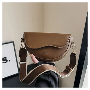 Détail d'un sac besace en cuir marron avec sangle tissée et boucles dorées