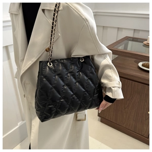Close-up of black quilted shoulder bag with chain strap styled on a beige trench coat