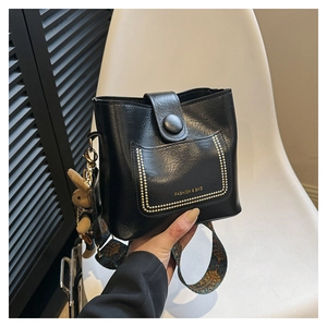 Detail of black leather bucket bag featuring gold rivets and bohemian woven strap