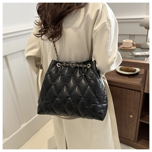 Close-up of black quilted bucket bag with gold chain strap on a wooden side table