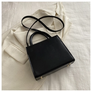 Détail d'un sac à main noir minimaliste avec pieds dorés et doubles poignées