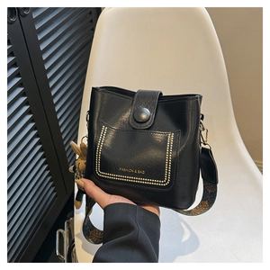 Detail of black leather bucket bag with gold studs, wide strap and plush bunny charm