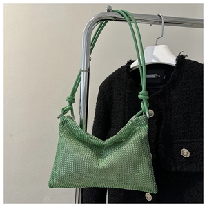 Detail der grünen Strass-Schultertasche mit Knotengurt vor einem Tweed-Jacken-Hintergrund