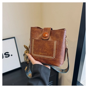 Close-up of retro brown bucket bag featuring gold studs and a colorful woven strap