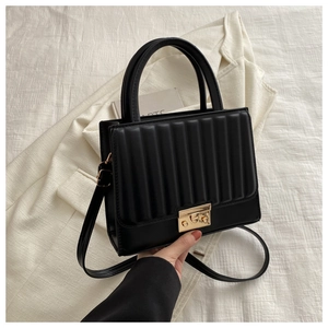 Détail d'un sac bandoulière plissé noir avec fermoir doré sur une veste blanche