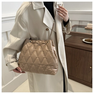 Beige quilted bucket bag with gold chain strap worn by a woman in a trench coat