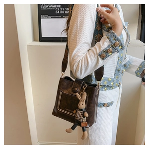 Close-up of brown faux leather bucket bag with ethnic embroidery strap and rabbit charm