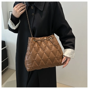 Close-up of brown quilted bucket bag featuring a gold chain strap and padded leather texture