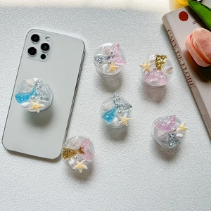 Detail view of glittery mermaid and seashell phone grips with pearls on a white phone