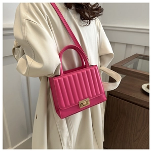 Sac bandoulière rose fuchsia avec rabat matelassé et fermoir doré porté sur un manteau