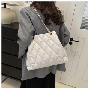 Detail of white quilted tote bag with metallic chain strap shown on model shoulder