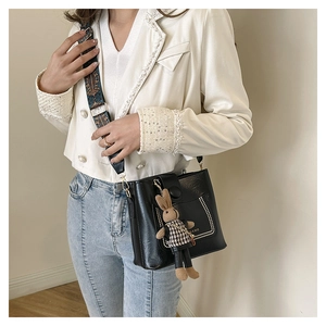 Detail of black leather bucket bag with floral wide strap and cute rabbit pendant