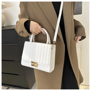 Détail du sac blanc plissé avec fermoir doré sur une tenue de tailleur marron