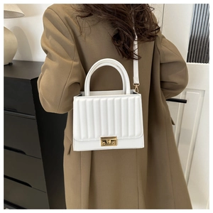 Détail d'un sac à main blanc matelassé avec fermoir doré porté par un mannequin