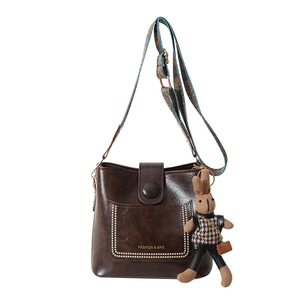 Retro dark brown bucket bag with wide ethnic strap and bunny charm on white background