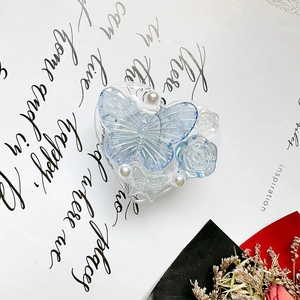 Detailed macro view of heart-shaped phone grip with blue butterfly, rose, and pearls