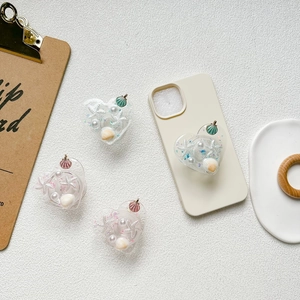 Détail d'un support de téléphone en cœur avec paillettes, coquillages et perles