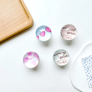 Detailed view of four round glass phone grips with pink hearts and text on a white desk