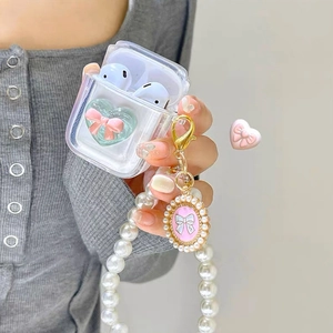 Detail of clear AirPods case with green heart, pink bow, and large pearl handle strap