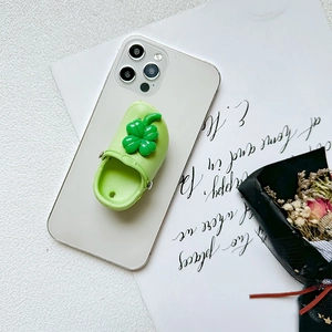 Green clog shoe phone stand with lucky clover charm on white smartphone back