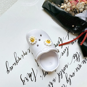 Close-up of white EVA clogs with cute yellow smiley daisy flower charms and airy vents