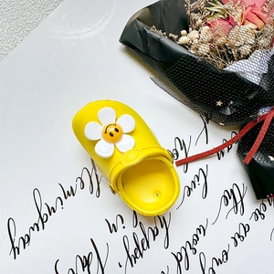 Close-up of a yellow EVA clog shoe featuring a large white flower and smiley face charm