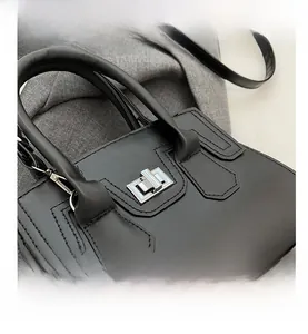 Detail of black matte handbag featuring silver twist-lock closure and decorative stitching