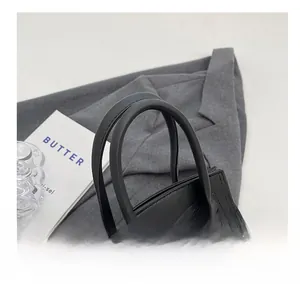 Detail of black leather handbag featuring thick double handles and a silver metal buckle