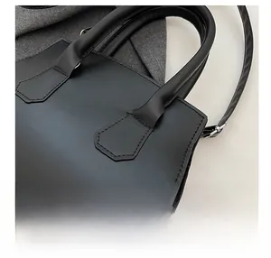 Detail showing smooth black leather texture and stitched reinforced handles of the handbag
