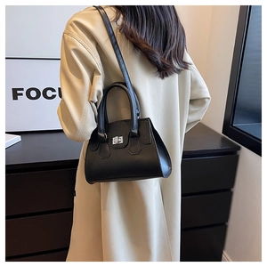Close-up of black minimalist crossbody bag with silver twist lock on a female model
