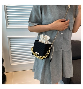 Detail of black textured mini crossbody bag with cream drawstring and gold chain handle