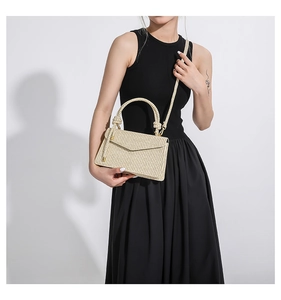 Detail of beige straw woven handbag with top handle and strap styled on a black dress