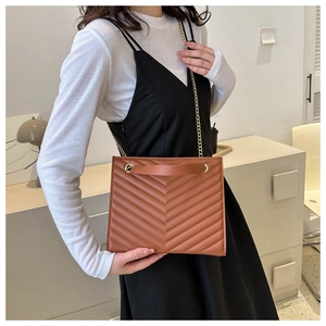 Detail of a brown quilted tote bag with V-shaped stitching and gold chain strap