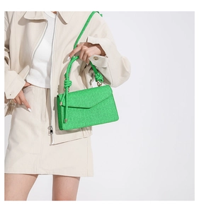 Detail of bright green woven crossbody bag with knotted handle and gold metal accents