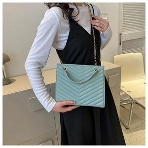 Detail of mint green quilted tote bag with golden metal chain strap and leather handle