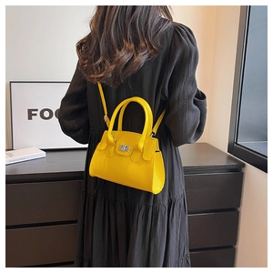 Detail of yellow matte leather handbag with silver lock worn with a black dress