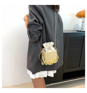 On-body view of woven straw bucket bag with gold chain strap and drawstring inner