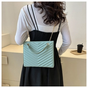 Detail of mint green tote bag featuring quilted chevron texture and gold chain strap