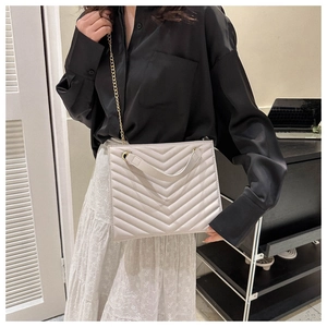 Detailed close-up of a white chevron quilted tote bag with golden chain straps on model