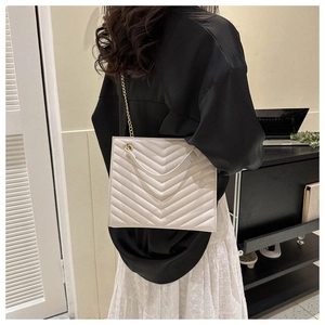 Detail of cream-white square shoulder bag with V-quilted texture and gold chain strap
