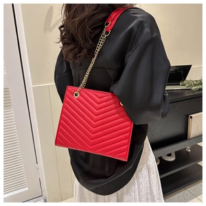 Detail of red quilted tote bag with V-shaped stitching and golden chain strap