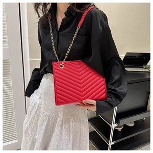 Detail of red quilted shoulder bag with gold chain strap worn by a model in casual style